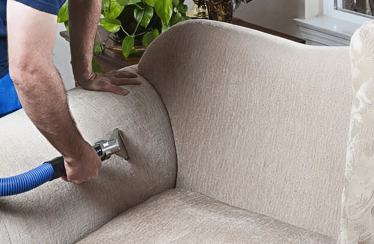 Professional upholstery cleaner deep-cleaning a fabric sofa with a handheld extraction tool and hose, Scottsdale, AZ.